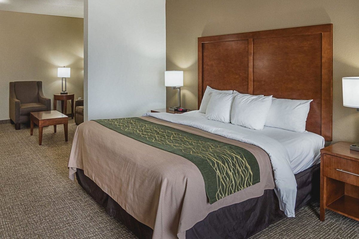 A hotel room with a large bed, a chair, a small table, and two bedside lamps.
