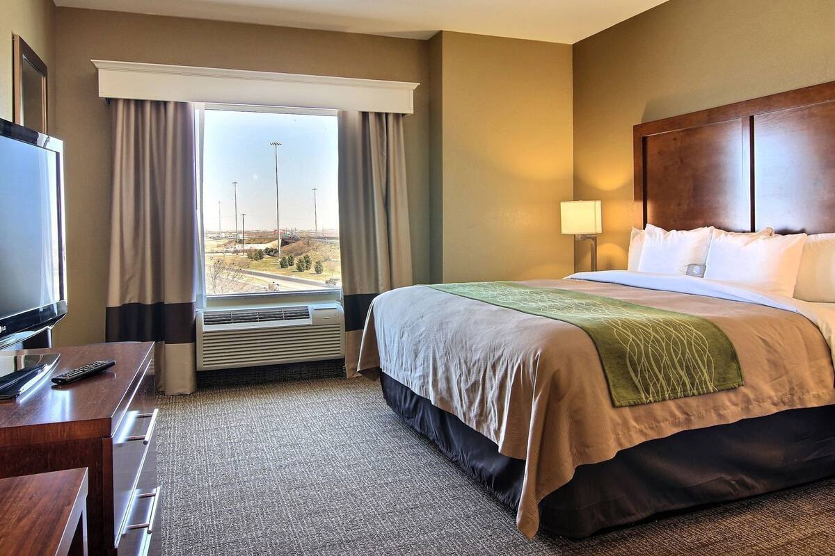 A hotel room with a bed, a TV, a desk, and a window with curtains.