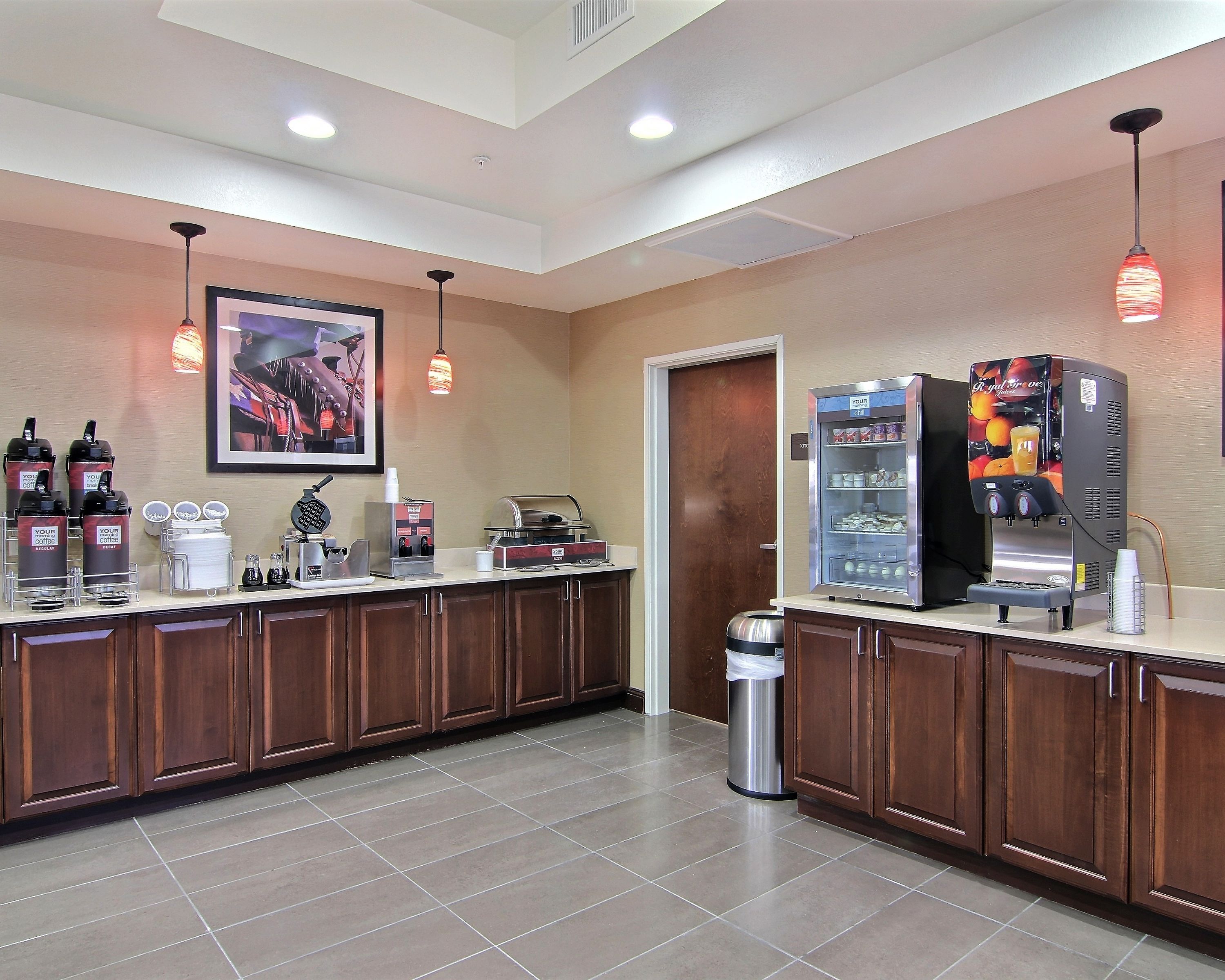 Uma área de recepção de hotel com um espaço para café, um refrigerador com bebidas e uma lixeira.