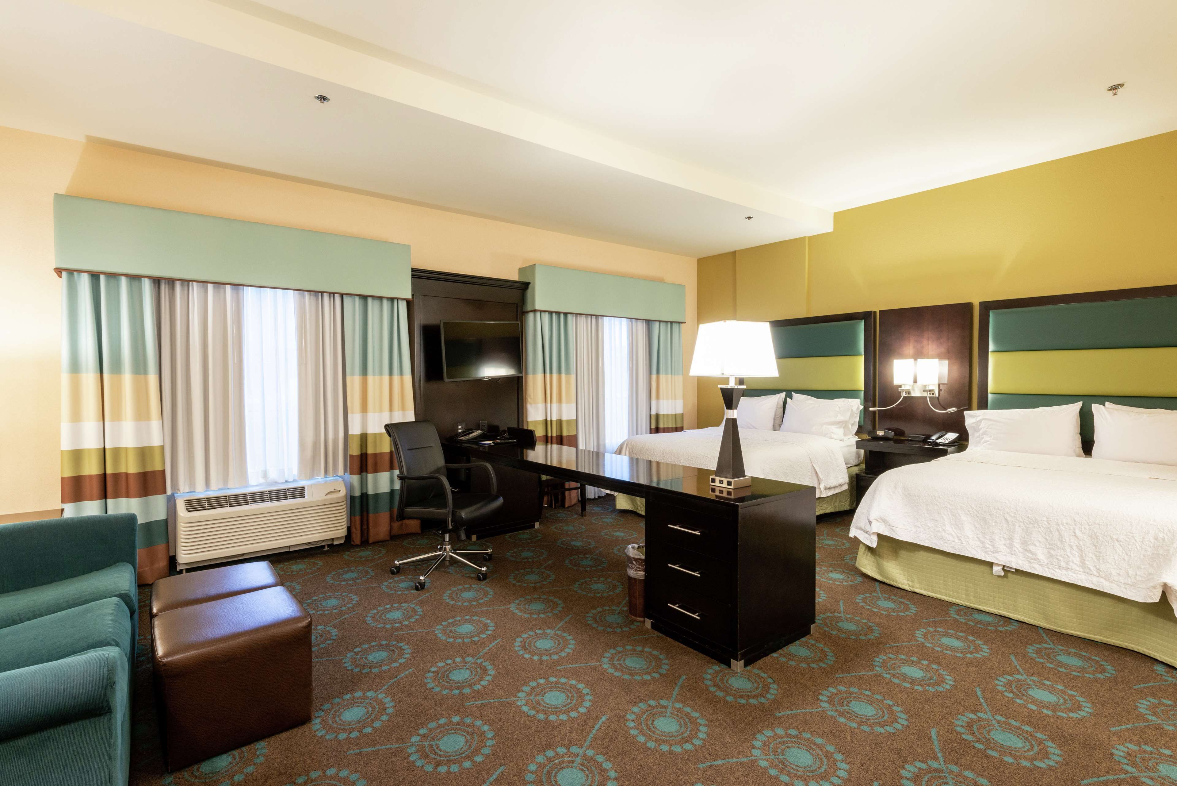 A hotel room with a bed, a desk, a chair, a dresser, and a TV.