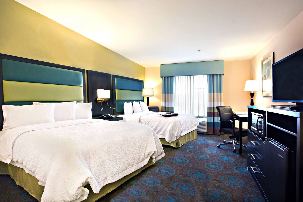 A hotel room with two beds, a desk, a chair, a television, and a desk lamp.