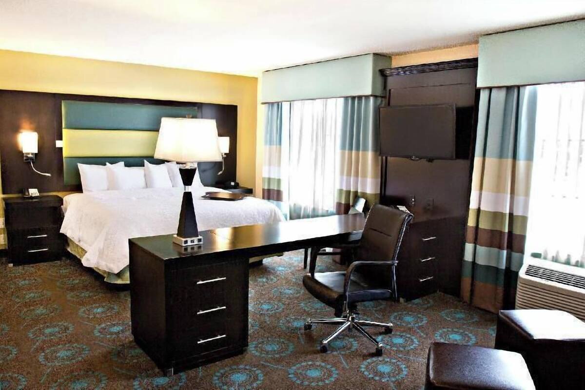 A hotel room with a bed, desk, chair, and a TV.