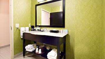A bathroom with a green wall, a black-framed mirror, a white countertop, and a sink. There are towels and toiletries on the counter.