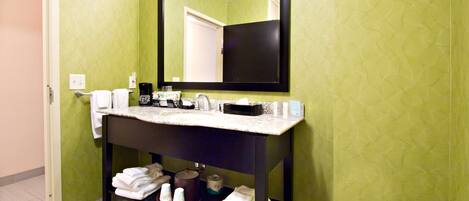 A bathroom with a green wall, a black-framed mirror, a white countertop, and a sink. There are towels and toiletries on the counter.