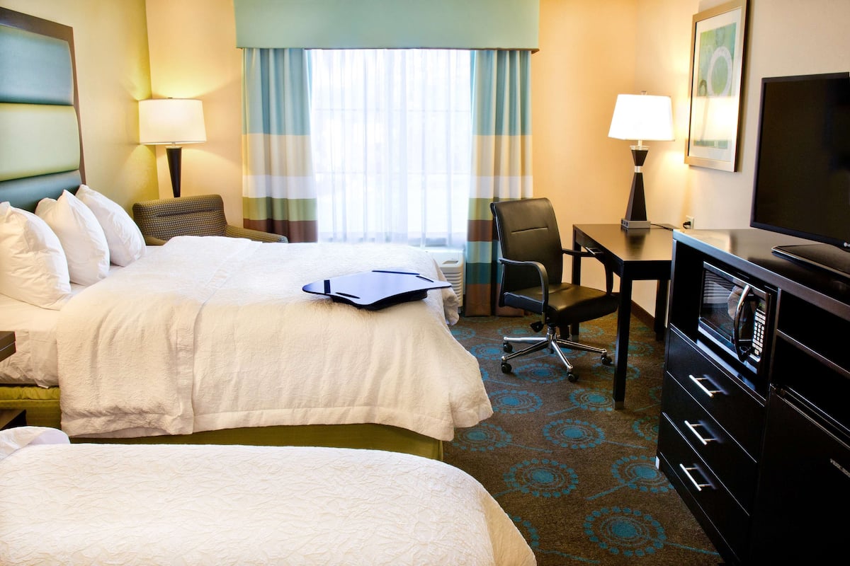 A hotel room with two beds, a desk with a chair, a television, and a lamp.