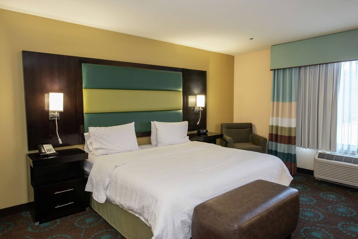 A hotel room with a large bed, two bedside tables, a chair, a desk, and a window with curtains.