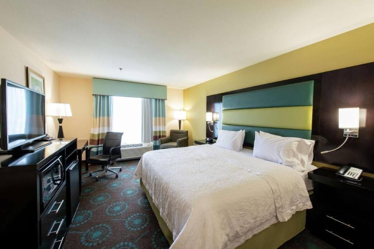 A hotel room with a bed, desk, chair, TV, and lamps.