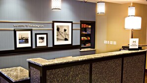 A reception area with a 'Welcome to Farmington' sign, framed pictures, a snack bar, and a Hilton Honors sign. - Hampton Inn & Suites Salt Lake City/Farmington (Farmington)
