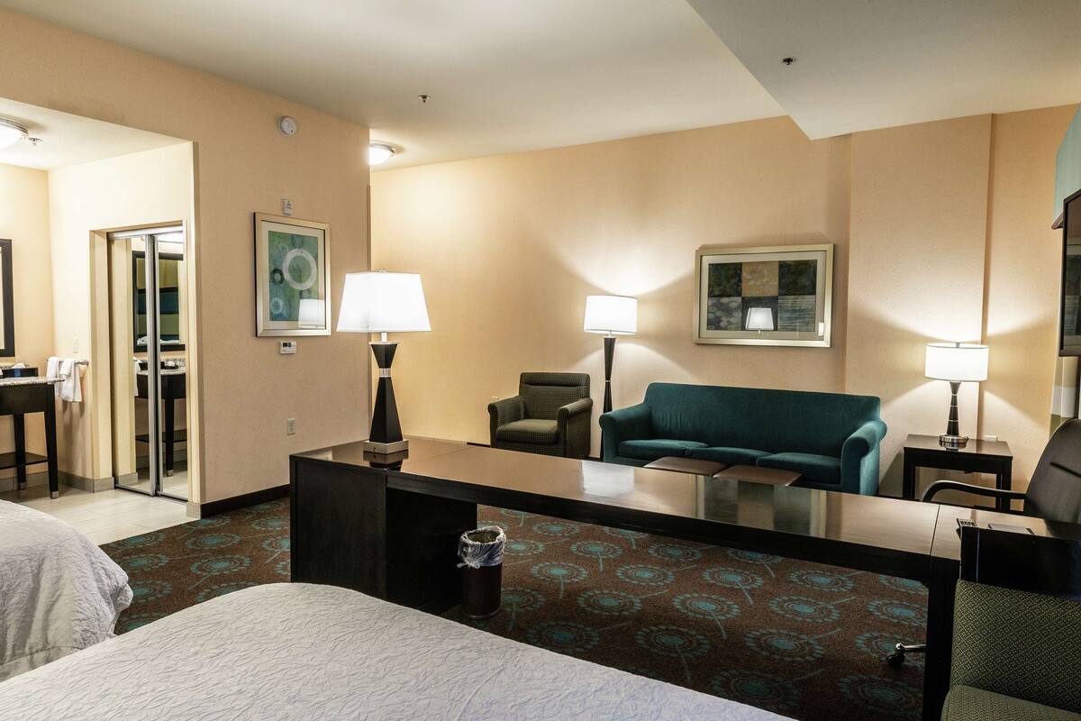A hotel room with a bed, a desk, a chair, a sofa, and a trash can.