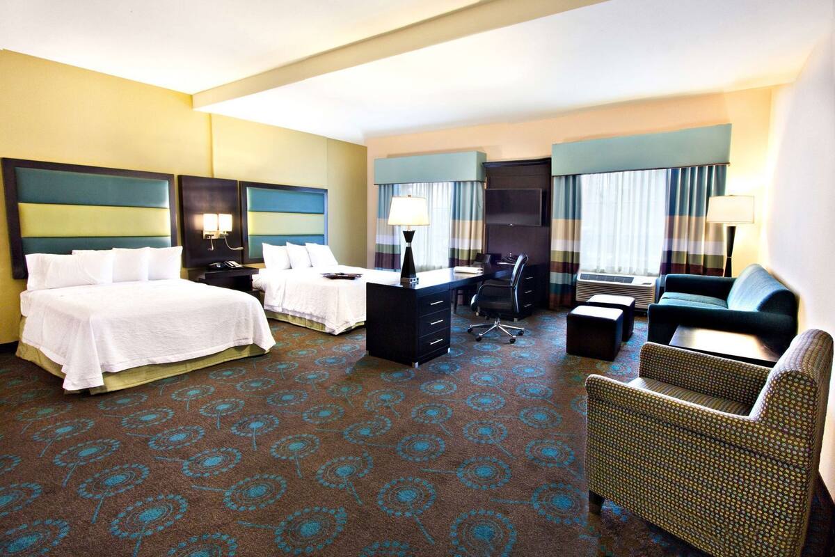 A hotel room with two beds, a desk, a chair, a sofa, and a TV.