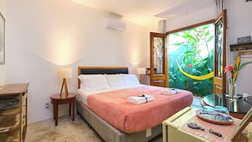 A neatly arranged bedroom with a bed, bedside tables, a dresser, and a view of greenery through the window.
