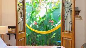 A hotel room with a bed, a wooden door leading to a garden, and a small table with a lamp. - Pousada Pontal Gardens (Paraty)