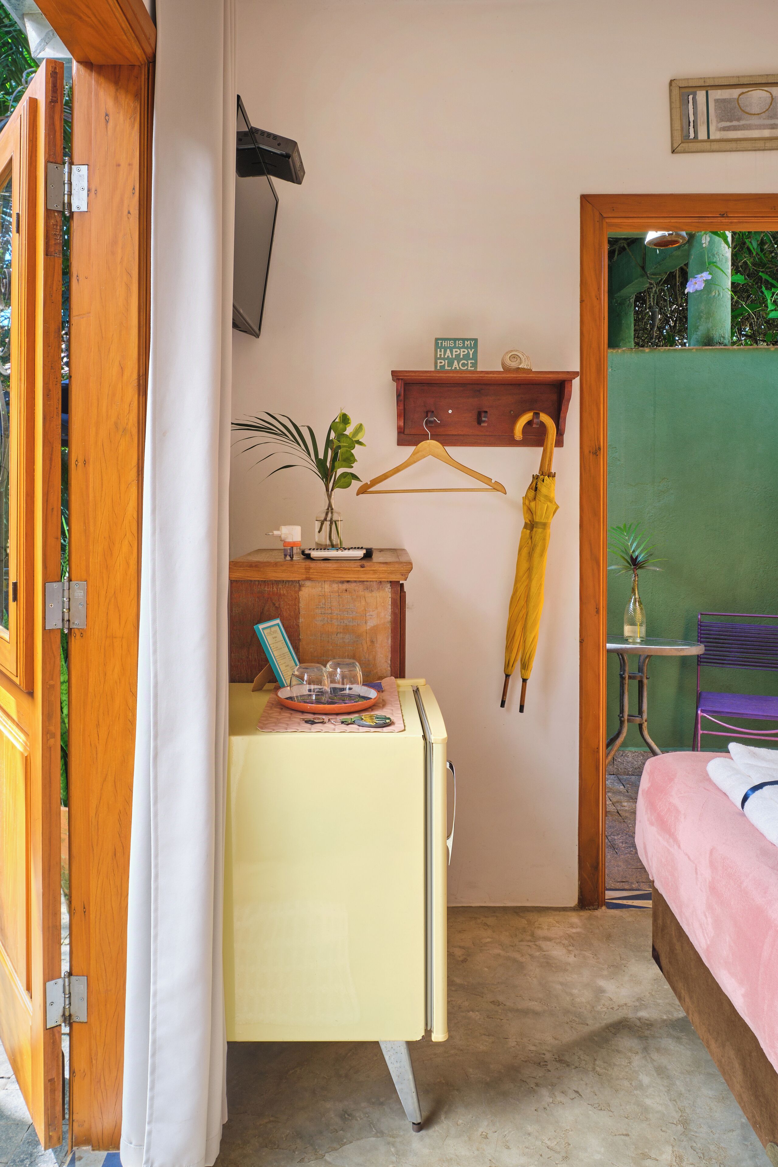 A compact room with a bed, a small table with a vase, and a desk with a plant and a keyboard.