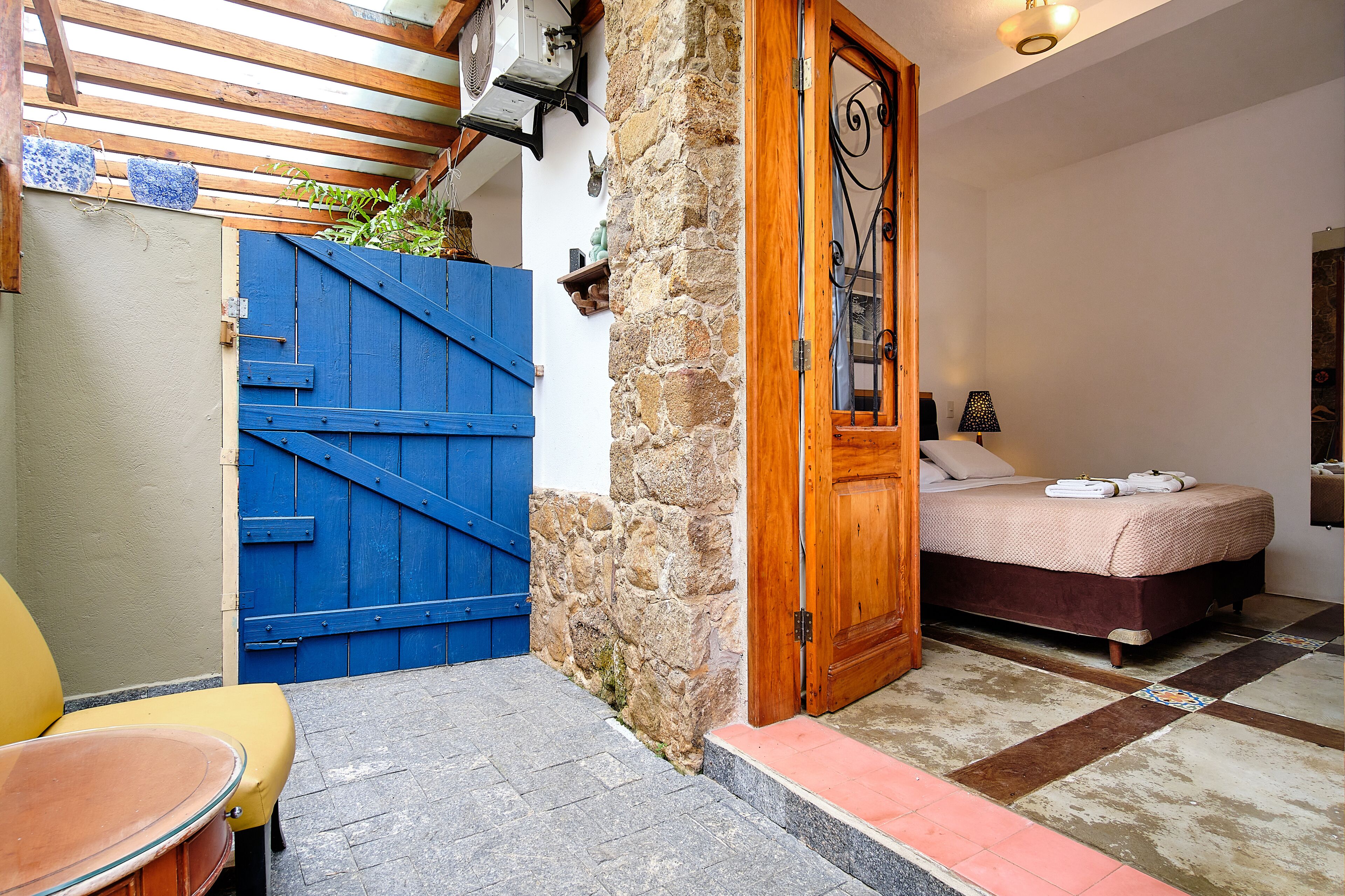 A room with a bed, a wooden door, a blue gate, and a stone wall.