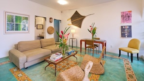 A living room with a beige sofa, a coffee table with books, a woven pouf, a patterned rug, and a wall-mounted decorative piece. - Pousada Pontal Gardens (Paraty)