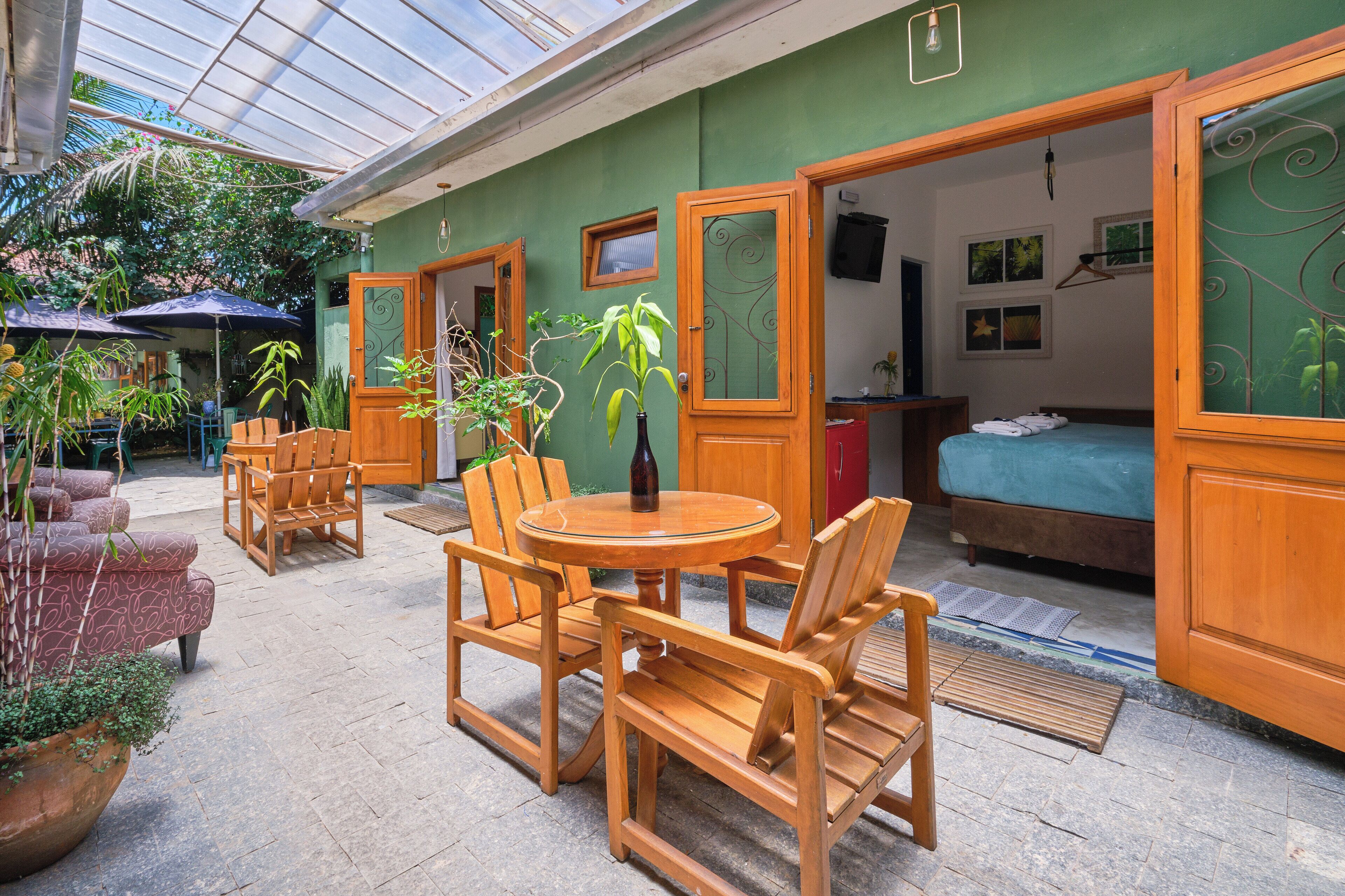 A room with a bed, a wooden table with chairs, and a potted plant.