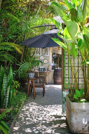 A garden pathway leading to a wooden table and chairs, surrounded by lush greenery and a large potted plant. - Pousada Pontal Gardens (Paraty)
