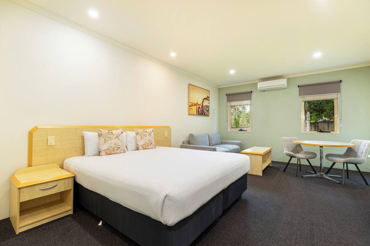 A hotel room with a large bed, a desk, two chairs, a small table, and a nightstand.