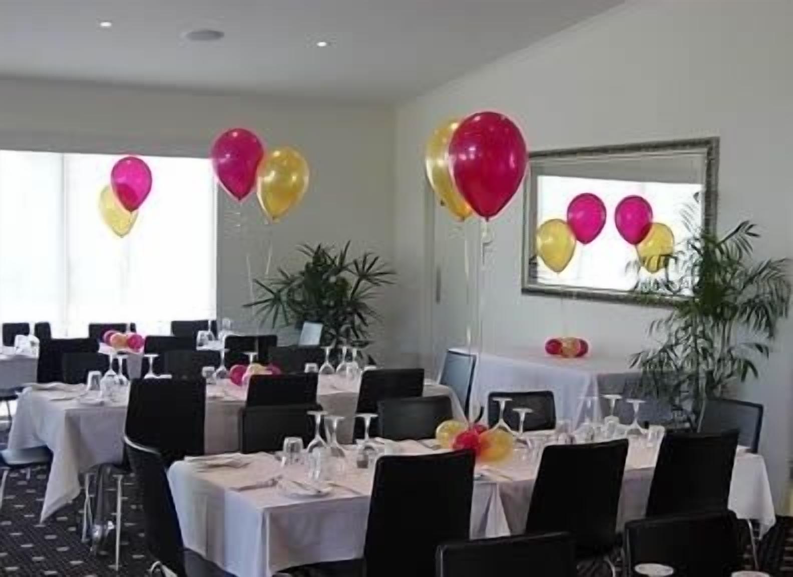 A dining area with tables set for a meal, balloons, and a large mirror on the wall.