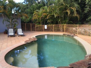 A swimming pool with a curved edge, surrounded by a tiled patio and a metal fence.