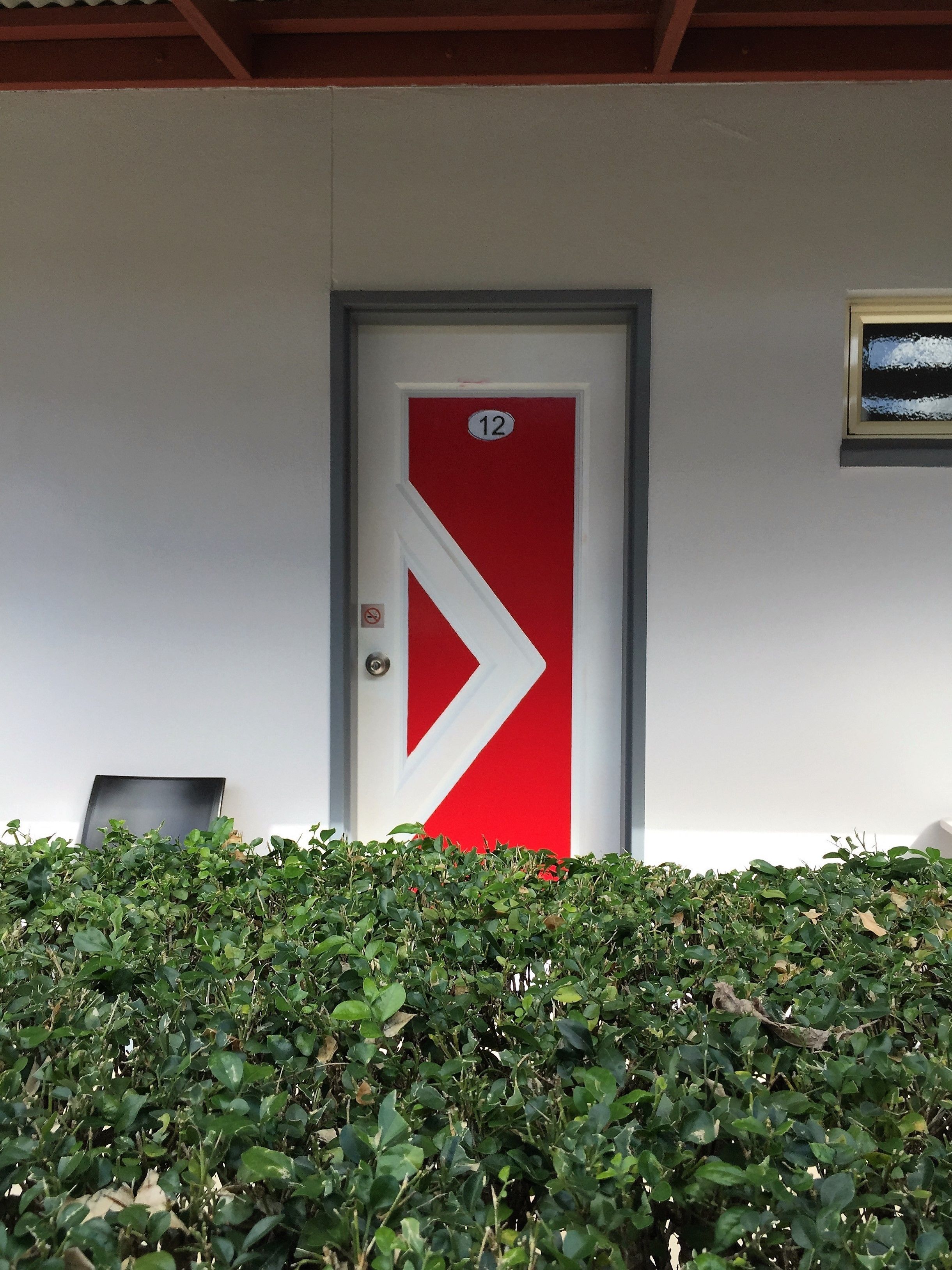 A door with a red and white arrow design, a number 12 sign, and a small no-smoking sign.