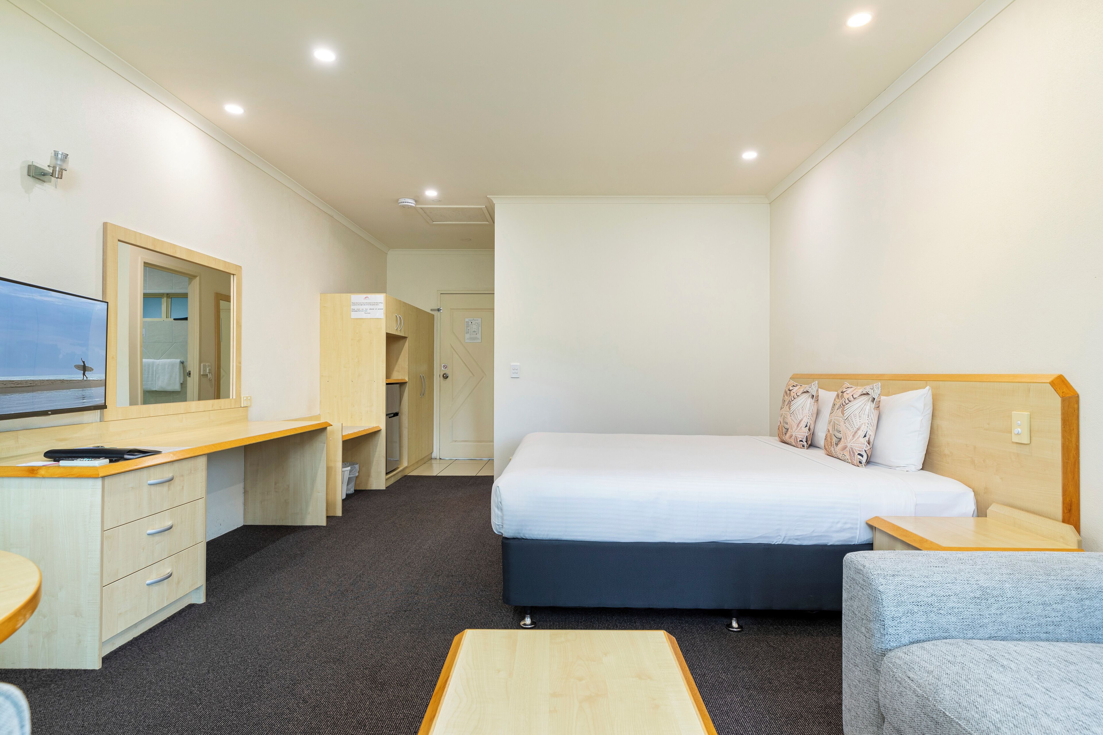 A hotel room with a bed, a desk, a chair, a TV, and a mirror.