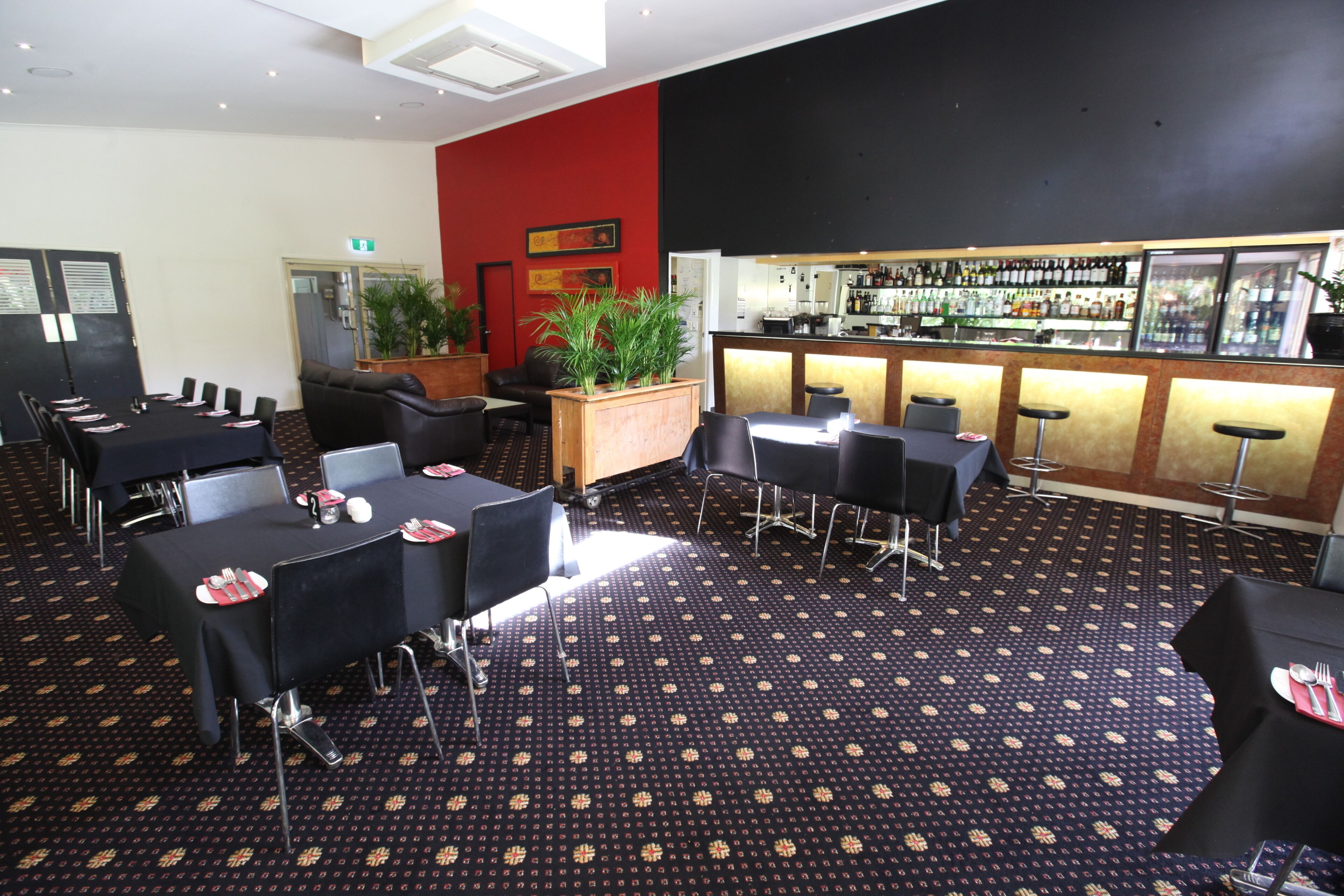 Eine Hotelhalle mit Barbereich, mehreren Tischen und Stühlen sowie einem gemusterten Teppich.