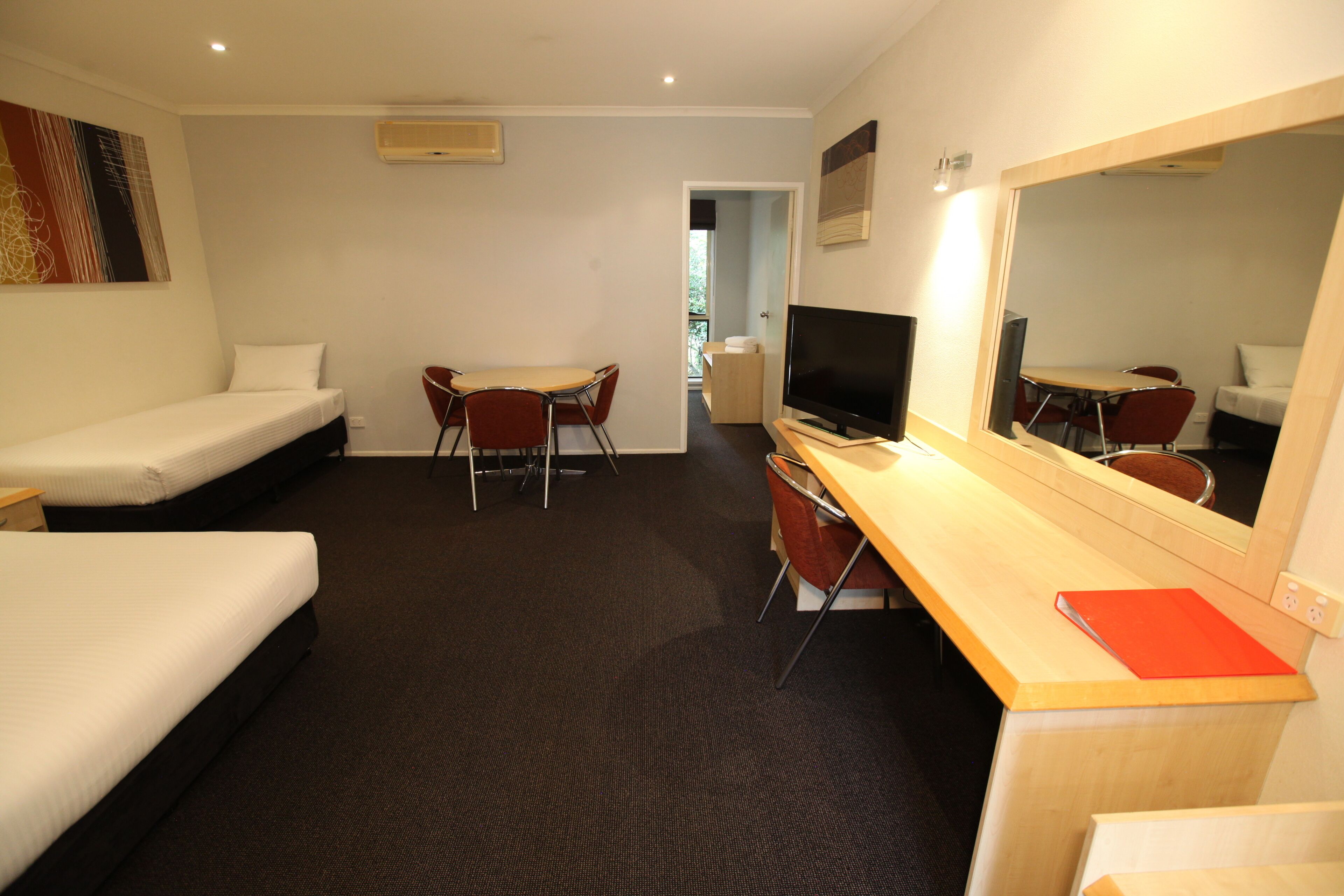 A hotel room with two single beds, a desk with a chair, a television, and a large mirror.
