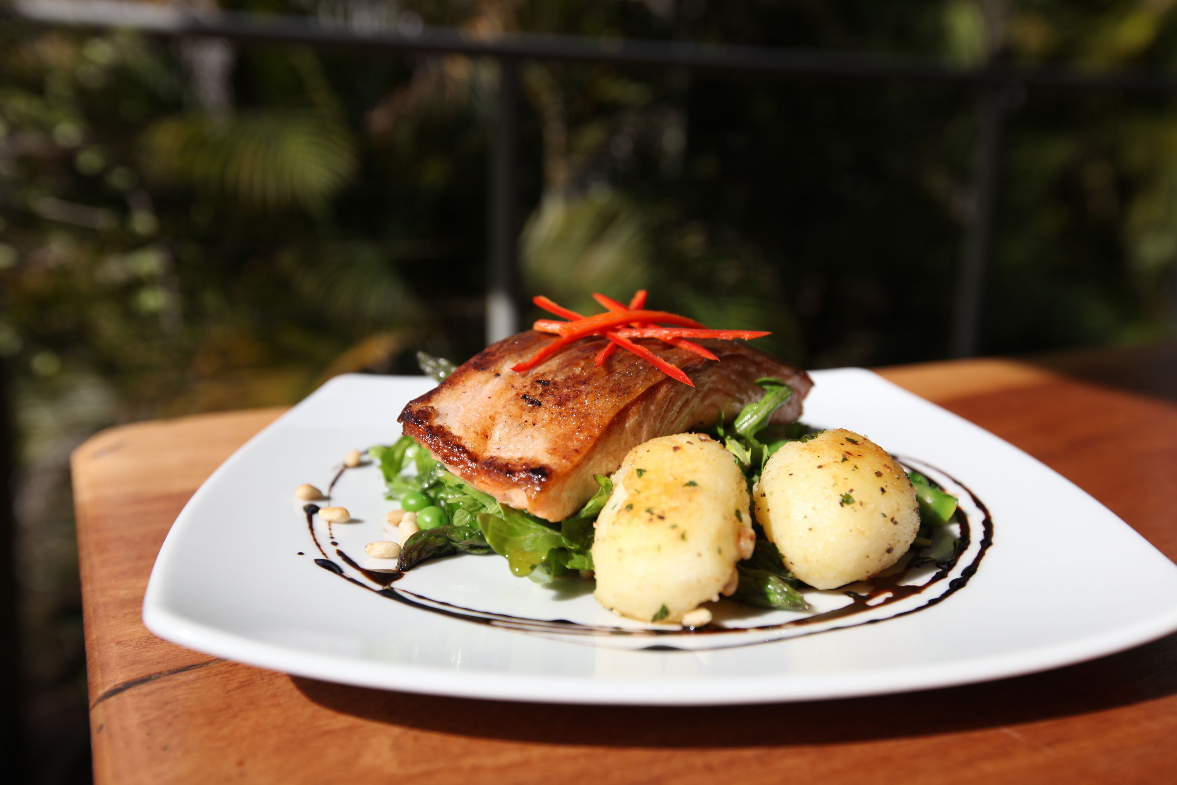 A plate of food with a piece of meat, two potatoes, and some greens on a white plate.
