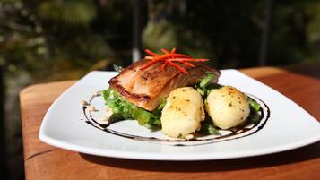 A plate of food with a piece of meat, two potatoes, and some greens on a white plate.