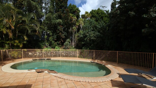 A swimming pool with a tiled deck, surrounded by a fence and trees. - Red Bridge Motor Inn (Woombye)