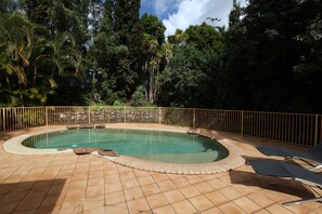 Una piscina con borde de baldosas, rodeada por una valla y árboles.