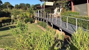 A restaurant with a covered outdoor seating area, surrounded by lush greenery and a wooden deck. - Red Bridge Motor Inn (Woombye)