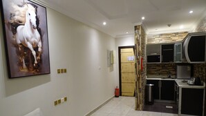 Uma sala de estar moderna com um sofá branco, um quadro abstrato grande e uma área de cozinha com micro-ondas e cafeteira.