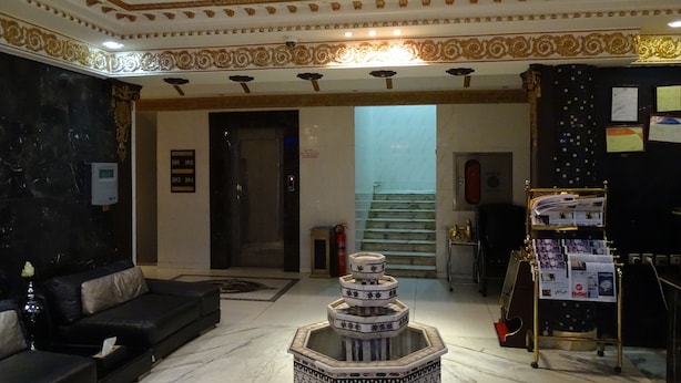 Um hall com um sofá de couro preto, uma fonte de azulejos decorativos e um balcão de recepção com um mural de avisos.