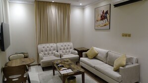 Uma sala de estar com sofá, poltronas, mesa de centro, televisão e um quadro na parede.