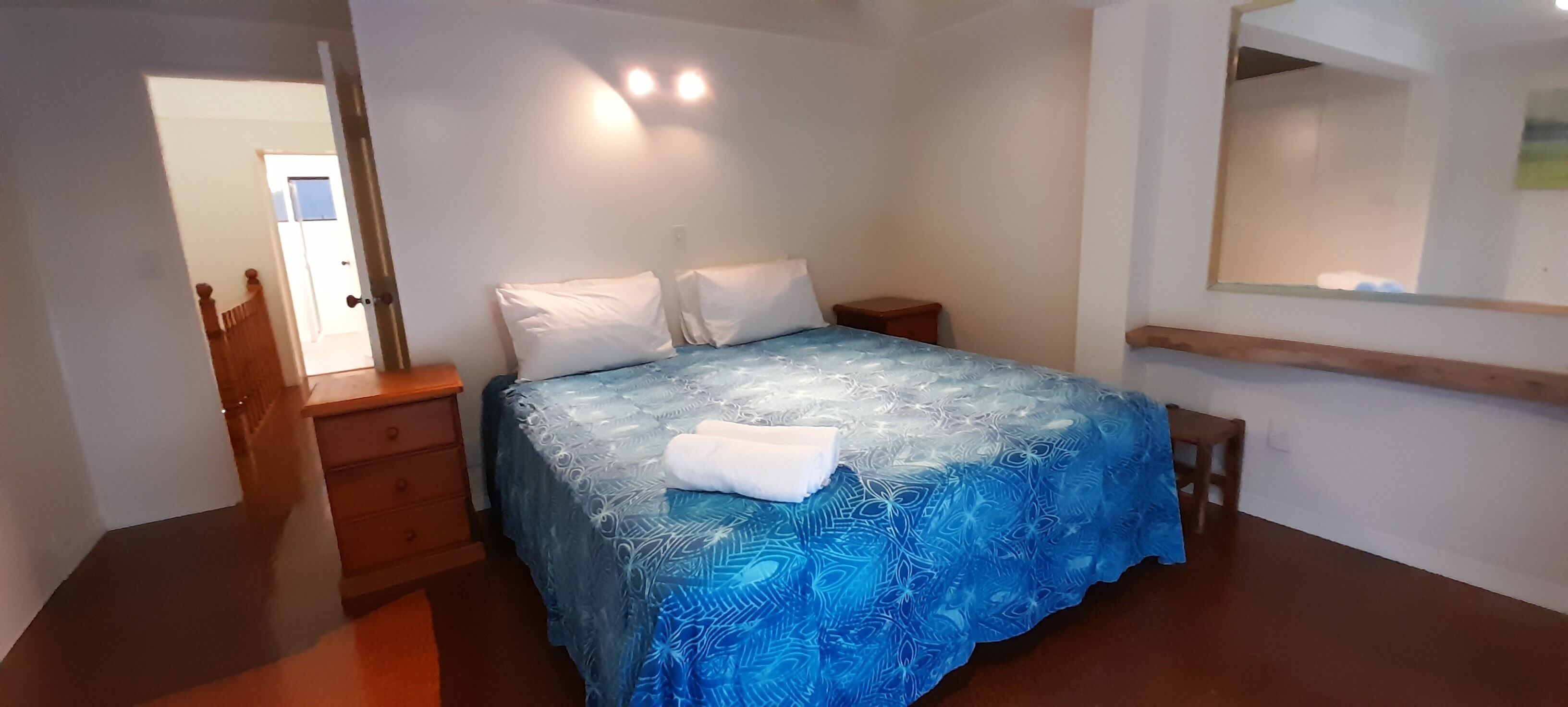 Un dormitorio con cama, mesitas de noche, cómoda, espejo y una puerta.