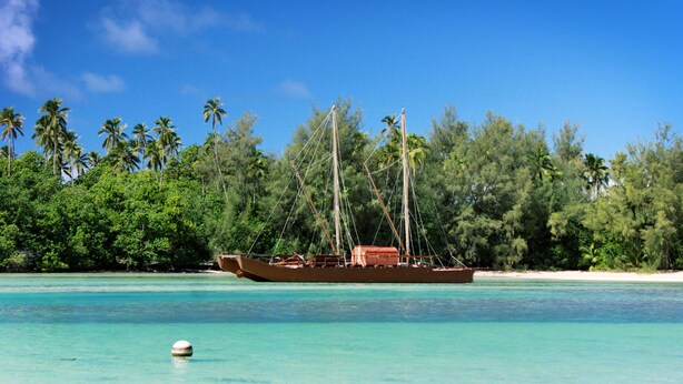 A boat on a turquoise sea with a beach and palm trees in the background. - Avana Waterfront Apartments (Rarotonga)