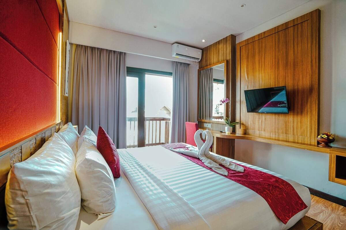 Une chambre d’hôtel dotée d’un grand lit, d’un téléviseur à écran plat fixé au mur, d’un balcon avec vue et d’un système de climatisation.