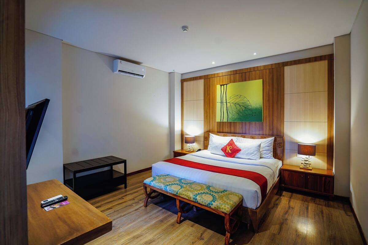 Une chambre d’hôtel équipée d’un lit, de lampes de chevet, d’un banc, d’une télévision et d’un appareil de climatisation.