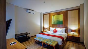A hotel room with a bed, bedside lamps, a bench, a TV, and an air conditioning unit.