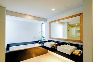 A modern bathroom with a large mirror, two sinks, a bathtub, and a potted orchid.