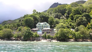 A multi-story house with a balcony, surrounded by lush greenery and a rocky hillside. - Treasure Cove (Mahé Island)