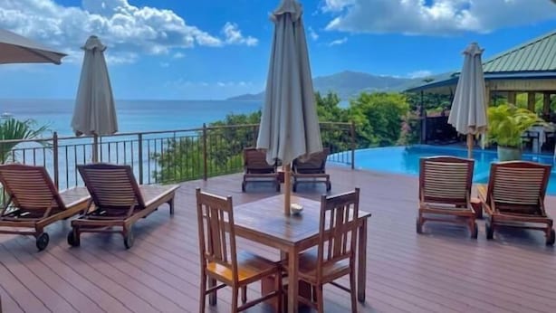 A wooden deck with outdoor seating and umbrellas overlooking a pool and ocean view. - Treasure Cove (Mahé Island)
