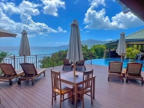 A wooden deck with outdoor seating and umbrellas overlooking a pool and ocean view. - Treasure Cove (Mahé Island)