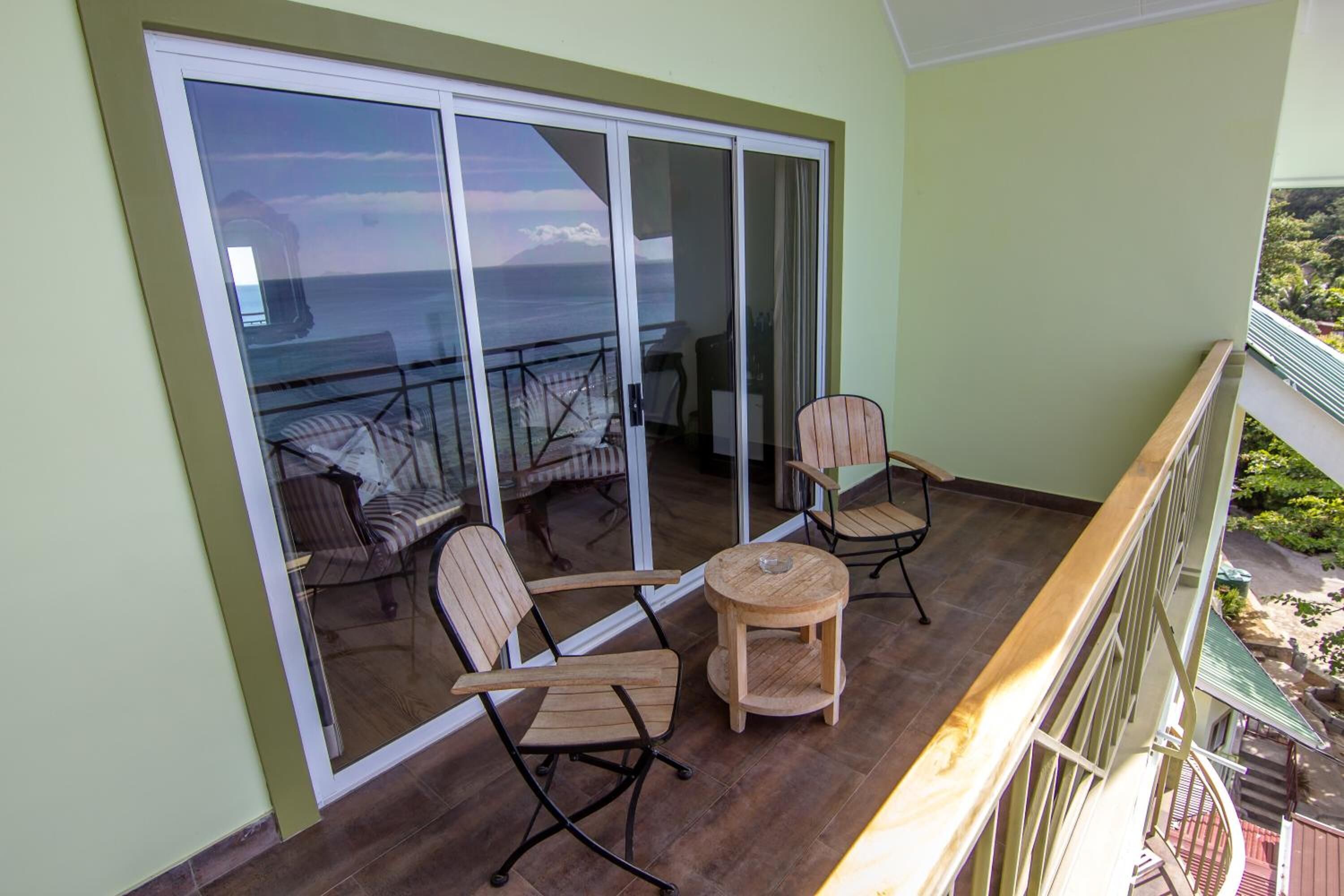 A balcony with two wooden chairs and a small round table, overlooking a scenic view of the ocean and a mountainous landscape.