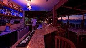 A bar area with a counter, shelves of bottles, and a view of the ocean at dusk. - Treasure Cove (Mahé Island)