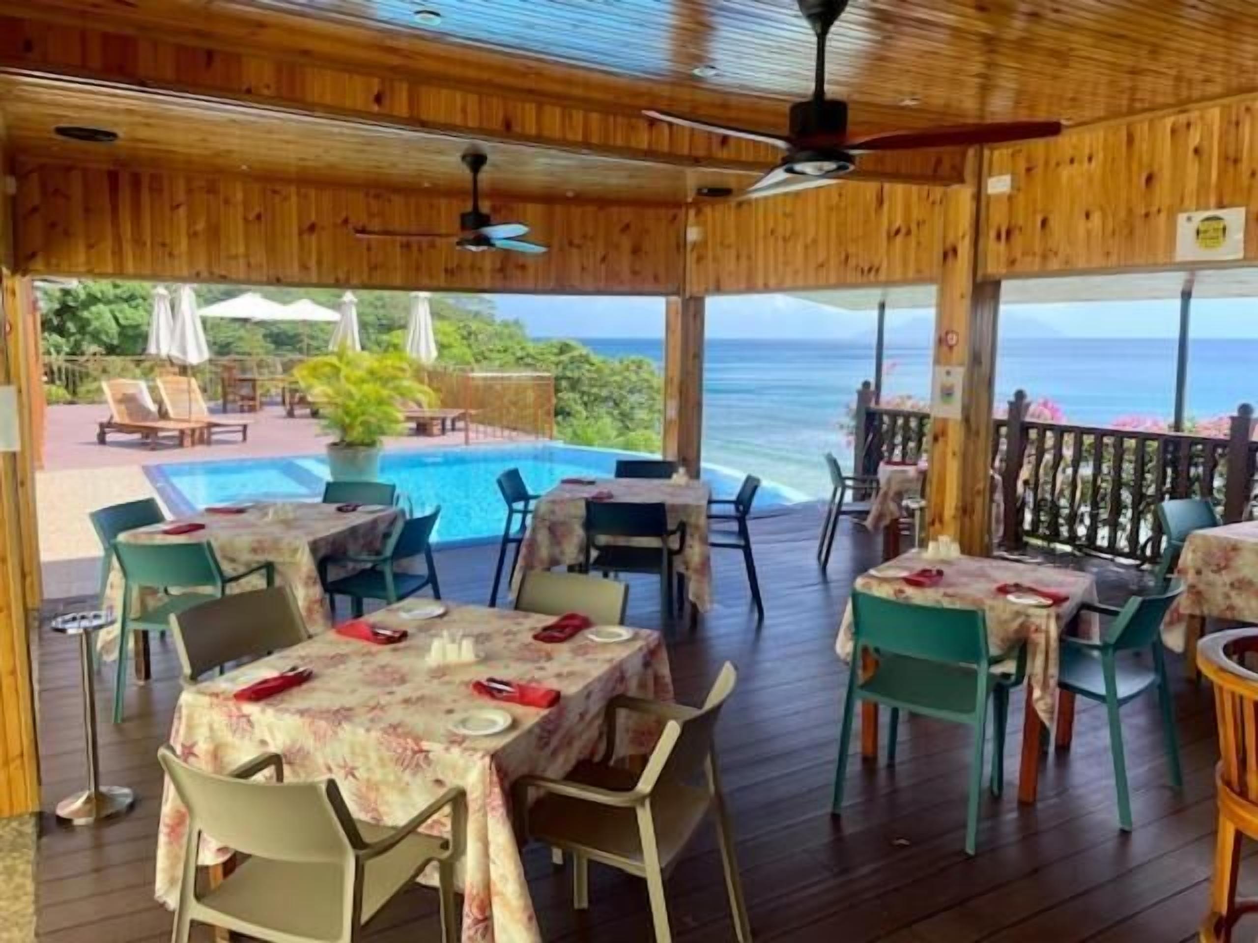 A restaurant with outdoor seating overlooking a pool and the ocean.