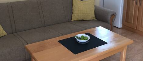 Un salon avec un canapé, une table basse sur laquelle se trouve un saladier rempli de fruits, et un tableau accroché au mur.