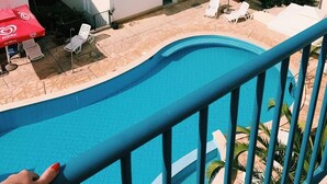 Zona de piscina con vista al mar, edificios blancos con tejados rojos y un paraguas rojo.